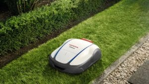 A robotic lawn mower on neatly trimmed grass beside hedges.